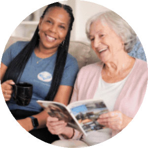 A companion and an older woman smiling while looking at a magazine together